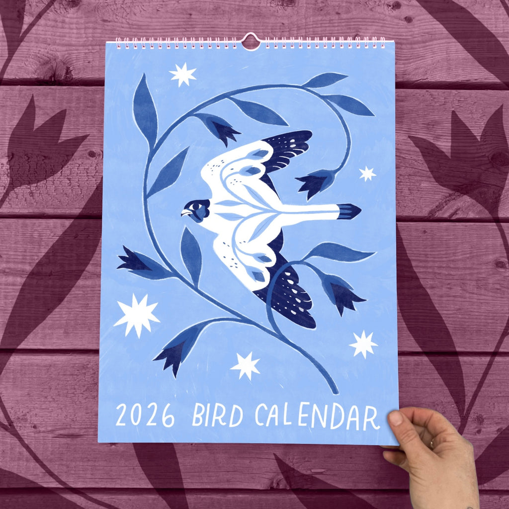 2026 Bird Calendar with a blue background and bird design held against a wooden surface.